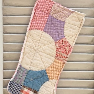 May include: A patchwork Christmas stocking with a pink, purple, blue, and orange color scheme. The stocking is made of quilted fabric and has a white background.