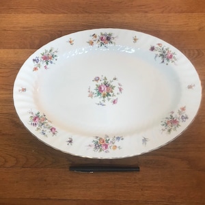 May include: White oval serving platter with a floral pattern in shades of pink, purple, and green. The platter has a scalloped edge.