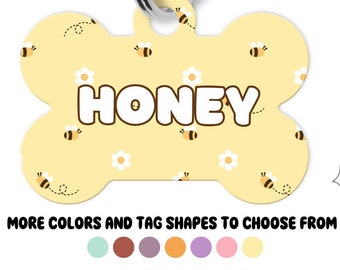 Puede incluir: Tres placas de identificación para mascotas de metal con anillas plateadas. Una placa en forma de corazón menta dice HONEY, una circular morada dice Bear y una en forma de hueso amarilla dice HONEY. Patrones de abejas y flores. Texto: MORE COLORS AND TAG SHAPES TO CHOOSE FROM.