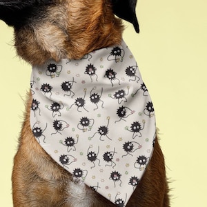 May include: A brown and black dog wearing a white bandana with a black and white pattern of small creatures. The dog is sitting on a white surface and looking up.