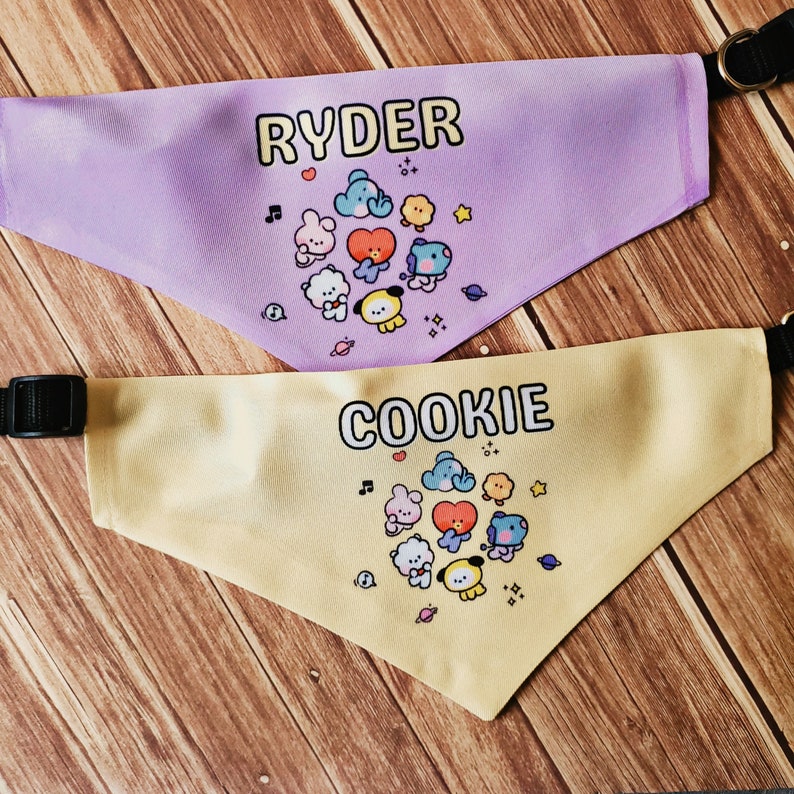 May include: Two yellow and purple dog bandanas with a cartoon character design. The bandanas are personalized with the names "Ryder" and "Cookie".