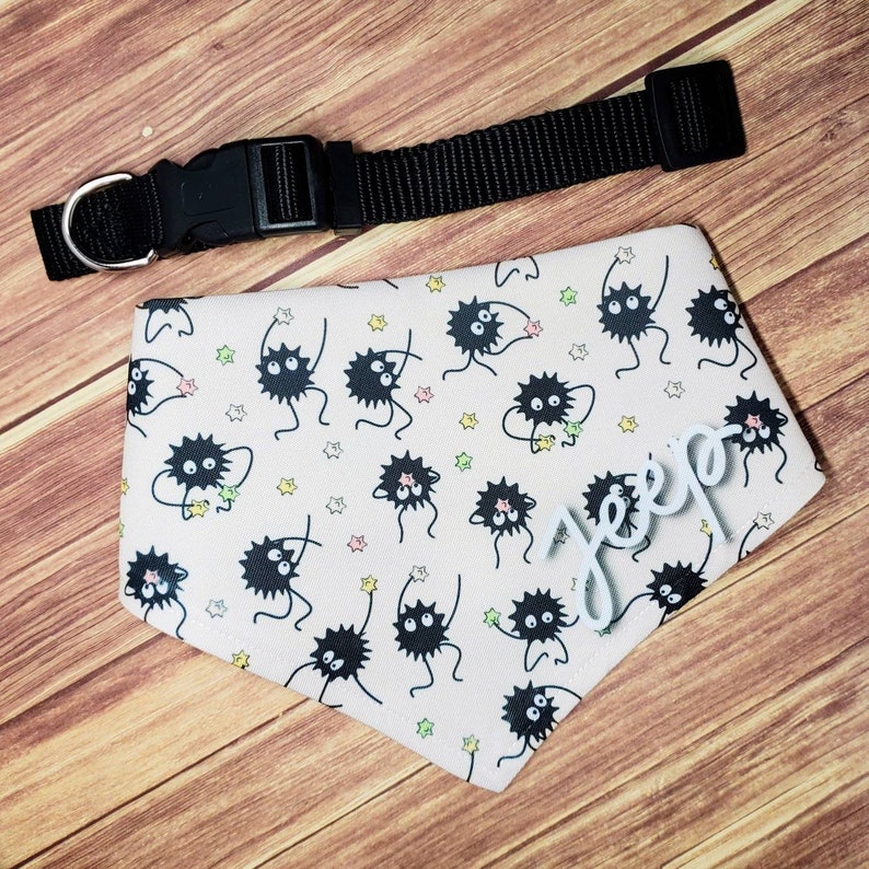 May include: A pink dog bandana with a black and white print of cartoon characters. The bandana has a white name tag that says "Jepp" on it.