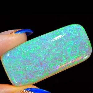 Może przedstawiać: Prostokątny zielony i biały opal szlachetny. Opal ma błyszczącą, tęczową powierzchnię.