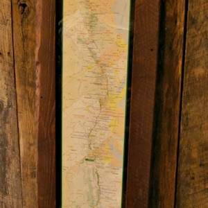May include: A rustic wooden frame with a map of the Appalachian Trail inside. The map is printed on paper and shows the trail's route from Georgia to Maine. The frame is dark brown and has a rough, textured surface.