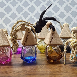 May include: A collection of small, colorful perfume bottles with wooden pyramid-shaped lids. Each bottle is a different color, including pink, blue, yellow, and brown. The lids are attached to the bottles with a rope. The word "Perfume" is printed on the lids.