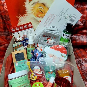 May include: A Christmas-themed gift box filled with various items. The box includes a Santa Claus illustration, socks with "BELIEVE" printed on them, a body scrub, soap, lip balm, and other festive accessories. The box is lined with red tissue paper.
