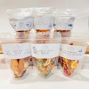 May include: Six clear plastic pouches containing various fruit and spice blends for simmering in a pot. The pouches are labelled with the Copper Kitchen logo and the names of the blends: Apple Pie, Sour Cherry & Rhubarb Crumble, Christmas Morning, Spiced Pear, Citrus Mint Breeze, and Cranberry Orange Bliss.