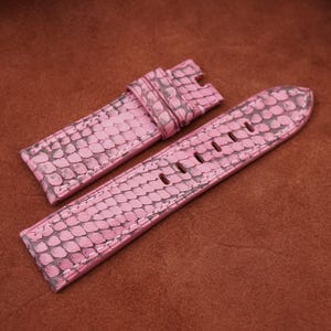 May include: Two pink leather watch straps with a textured snake skin pattern. The straps are laid out on a brown suede surface.