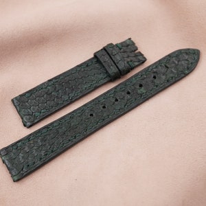 May include: Two dark green leather watch straps with a textured pattern. The straps are laid out flat on a light pink surface.