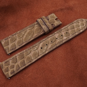 Puede incluir: Dos correas de reloj de cuero marrón con un patrón de cocodrilo. Las correas están dispuestas sobre una superficie marrón.