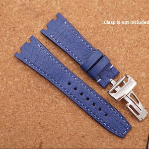 Könnte beinhalten: Ein blaues, strukturiertes Uhrenarmband mit weißen Nähten und einer silberfarbenen Metall-Faltschließe. Das Armband hat ein gekerbtes Ende zur Befestigung. Der Text Clasp is not included ist in der Nähe des Armbands sichtbar.