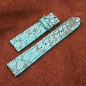 May include: Two turquoise leather watch straps with a textured pattern. The straps are laid out on a brown suede surface.
