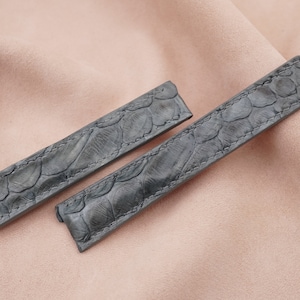 Könnte beinhalten: Zwei graue Lederarmbänder mit einem strukturierten Muster. Die Armbänder sind aus weichem, geschmeidigem Leder und haben einen klassischen Look.