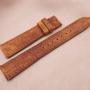 Könnte beinhalten: Ein braunes Lederarmband mit einem Wabenmuster. Das Armband ist aus echtem Leder und hat ein klassisches Design.