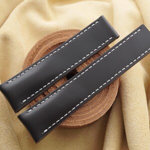 May include: Two black watch straps featuring a smooth matte finish and prominent white contrast stitching along the edges. The rectangular straps are positioned diagonally, showcasing a clean design with straight ends and a uniform width throughout.