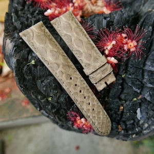 Puede incluir: Dos correas de reloj de cuero gris con un patrón texturizado. Las correas están dispuestas sobre una superficie gris oscuro texturizada.