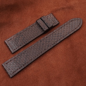 Op de afbeelding: Twee bruine leren horlogebandjes met een textuurpatroon. De bandjes liggen op een bruine suède ondergrond.