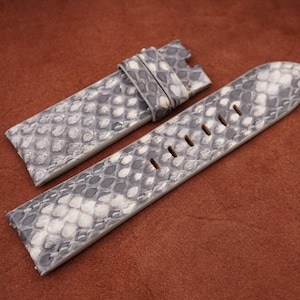 Puede incluir: Dos correas de reloj de piel de serpiente gris y blanca. Las correas están hechas de cuero genuino y tienen una superficie texturizada.