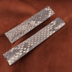 Könnte beinhalten: Zwei hellgraue Lederarmbänder mit Schlangenhautmuster.