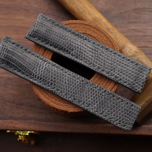 Peut inclure: Deux bracelets de montre en cuir gris avec un motif texturé ressemblant à du cuir d'alligator. Les bracelets sont posés sur une surface en cuir brun.