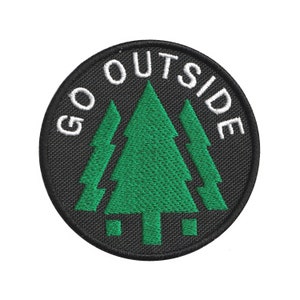 May include: Circular black patch featuring the text "GO OUTSIDE" in white, encircling three green stylized pine trees. The patch has a textured surface, and the design is set against a white backdrop.