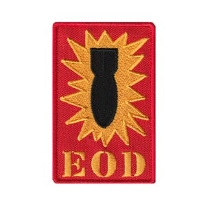May include: A rectangular embroidered patch with a red background. The center features a black bomb icon surrounded by a yellow starburst design. Below the graphic, the letters EOD are stitched in yellow thread with a bold, serif font style.