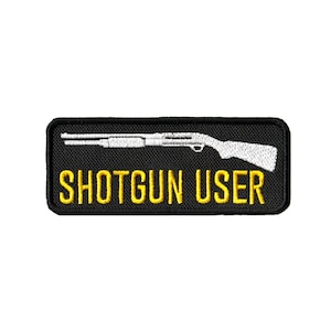 Pode incluir: Etiqueta bordada preta com uma silhueta branca de uma espingarda e o texto "SHOTGUN USER" em amarelo.