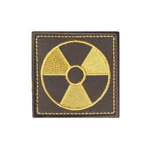 May include: A square-shaped embroidered patch featuring a dark brown fabric base with a yellow radiation hazard symbol stitched in the center. The patch has a matching yellow stitched border along the perimeter of the square fabric edge.