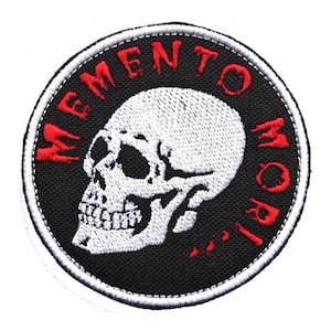 May include: A black and white embroidered patch featuring a white skull and the words "Memento Mori" in red.