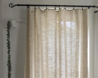 May include: A pair of off-white linen curtains hanging from a black metal curtain rod. The curtains are gathered at the top and hang straight down to the floor.