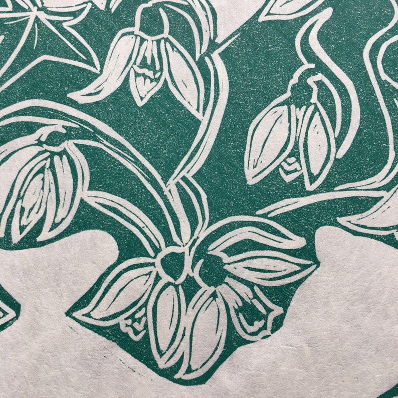 May include: A green and white linocut print of snowdrops. The print features a stylized design of the flowers with their stems and leaves.