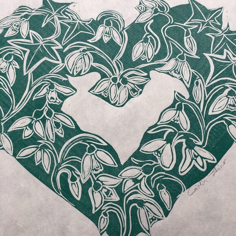 May include: A green heart-shaped print featuring white snowdrop flowers and leaves. The print is signed "Caitlin Fisher" in the bottom right corner.