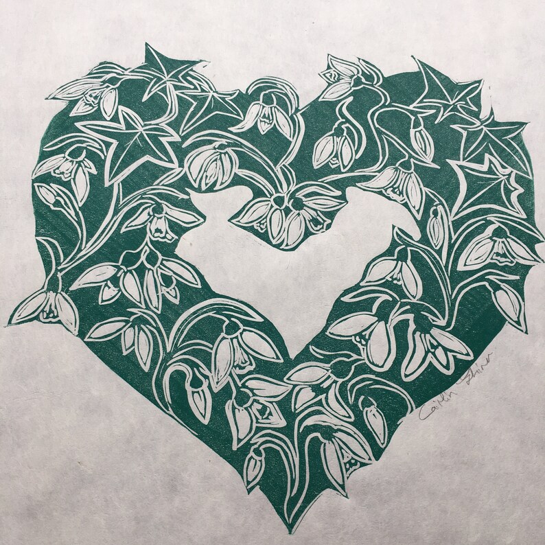 May include: A green heart-shaped print featuring a floral design with white snowdrop flowers. The print is signed "Caitlin Shearer" in the bottom right corner.
