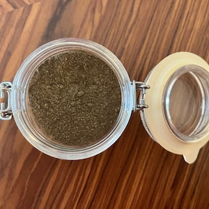 May include: A glass jar with a metal lid filled with brown powder. The lid is open and the jar is sitting on a wooden surface.