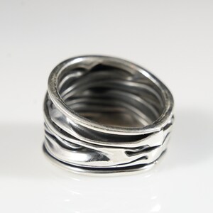 Könnte beinhalten: Ein silberner Ring mit einem strukturierten, geschichteten Design. Der Ring ist breit und hat einen einzigartigen, organischen Look.