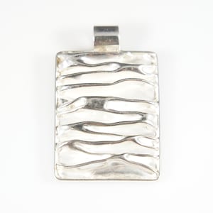 May include: Silver pendant with a textured, wavy design. The pendant is rectangular in shape and has a simple bail.