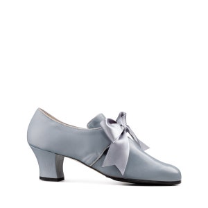 May include: A pale blue satin shoe with a bow. The shoe features a small heel and a rounded toe. The bow is made of matching satin. The shoe is a vintage design, reminiscent of a bygone era.