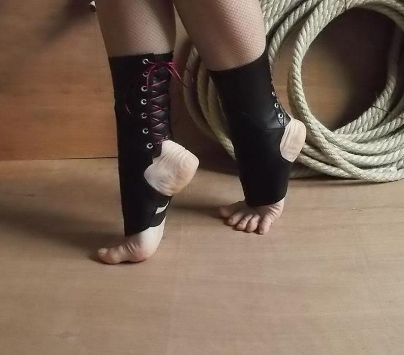 May include: A pair of black ankle spats featuring a lace-up design with silver-toned metal eyelets and thin dark red laces. These foot accessories cover the lower leg and ankle area, leaving the heel and toes exposed for a secure fit.