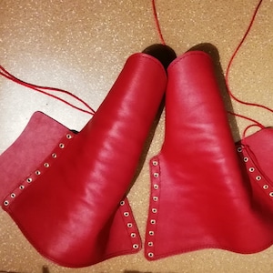 Peut inclure: Une paire de prot&egrave;ge-bras ou de jambi&egrave;res en cuir rouge vif, dot&eacute;e d'une s&eacute;rie d'&oelig;illets m&eacute;talliques sur les bords pour le la&ccedil;age. Chaque pi&egrave;ce est fabriqu&eacute;e en cuir rouge lisse et comprend de longs cordons rouges fins pour la fixation.