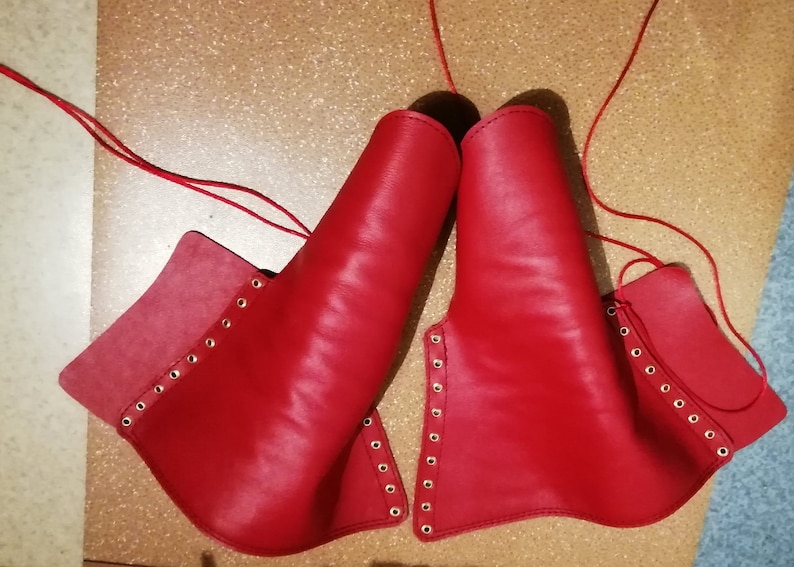 Peut inclure: Une paire de prot&egrave;ge-bras ou de jambi&egrave;res en cuir rouge vif, dot&eacute;e d'une s&eacute;rie d'&oelig;illets m&eacute;talliques sur les bords pour le la&ccedil;age. Chaque pi&egrave;ce est fabriqu&eacute;e en cuir rouge lisse et comprend de longs cordons rouges fins pour la fixation.