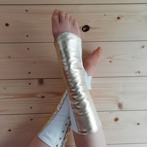 May include: A pair of white and gold leg warmers with a lace-up detail. The leg warmers are made of a soft, stretchy material and are perfect for adding a touch of style to any outfit.