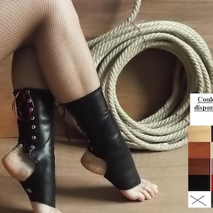May include: Black leather ankle wraps featuring a lace-up front with silver-toned metal eyelets and red laces. The design includes an open heel and toe area. A color chart is displayed on the right with the text Couleurs disponibles.