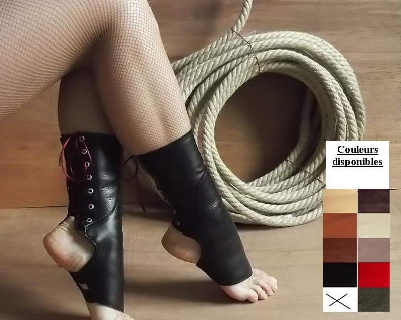 May include: Black leather ankle wraps featuring a lace-up front with silver-toned metal eyelets and red laces. The design includes an open heel and toe area. A color chart is displayed on the right with the text Couleurs disponibles.