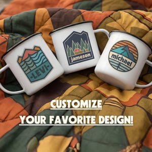 May include: Three white enamel mugs with black rims and handles, each featuring a unique outdoor-themed design. One mug has "-LEVI-", another "jameson", and the third "michael". The mugs are on a colorful quilted blanket. The text "CUSTOMIZE YOUR FAVORITE DESIGN!" is also visible.