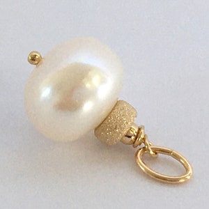 May include: A cream-colored, baroque pearl pendant with a gold-colored bail and accents. The pearl has a smooth, lustrous surface. The pendant is designed for jewelry making or as a charm. The gold-colored metal has a textured finish.