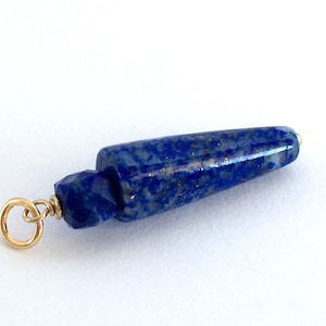 May include: A blue lapis lazuli pendant with gold wire wrapped around the top and a gold jump ring. The pendant is shaped like a long, thin point.