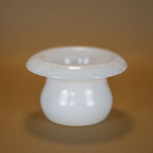 May include: A white ceramic vase shaped like a mushroom with a scalloped rim.