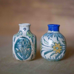 Peut inclure: Deux petits vases en céramique avec des motifs floraux bleus, verts et jaunes. Les vases sont blancs avec un glaçage craquelé.