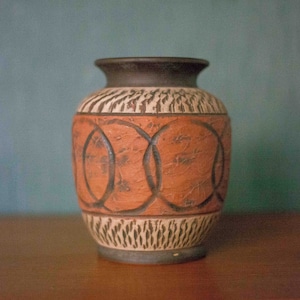 May include: A brown and white ceramic vase with a geometric pattern. The vase has a rounded body and a narrow opening.