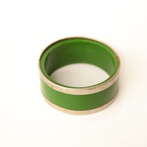 Peut inclure: Un anneau de serviette vert et argent. L'anneau est fait d'un matériau vert avec une bande argentée autour du haut et du bas.